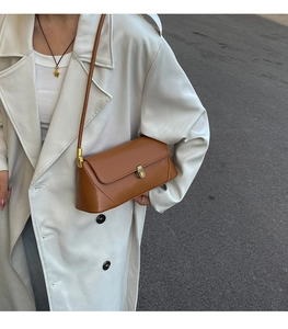 Sac baguette en cuir marron caramel avec boucle dorée porté à l'épaule sur un manteau