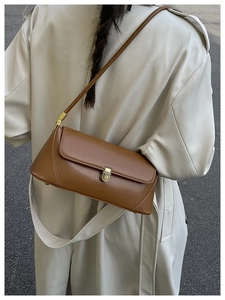 Sac baguette en cuir marron avec fermoir doré porté sur un trench-coat beige