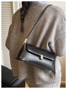 Détail d'un sac baguette noir avec boucle dorée porté sur un pull en maille grise