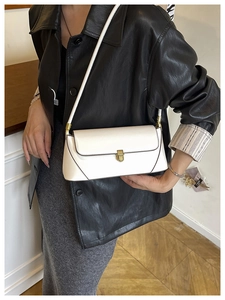 Gros plan d'un sac baguette en cuir crème avec fermoir vintage doré porté à l'épaule