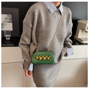 Detail of dark green acrylic clutch with gold wave metal trim and slim chain strap