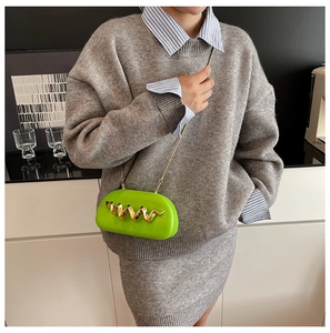 Detail view of bright green acrylic clutch bag with iconic gold wavy metal decoration