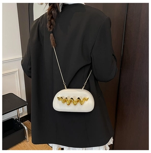 Detail of cream acrylic crossbody bag with gold wave metal decor on model in black blazer