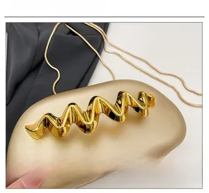 Detail of gold acrylic evening clutch with wave-shaped metallic hardware and snake chain