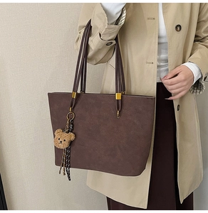 Détail du sac cabas mat marron foncé avec charm d'ours en peluche et garnitures dorées