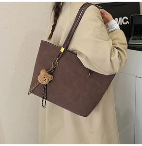 Détail d'un grand sac cabas marron mat avec un pendentif ours en peluche sur un mannequin
