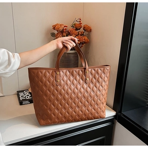 Detail of a brown quilted tote bag with diamond stitching and golden rivet accents