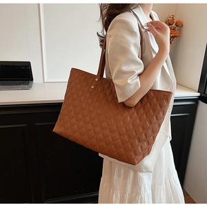 Detail view of brown quilted tote bag with fine stitching and gold rivet accents