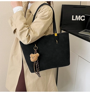 Détail du grand sac cabas noir mat avec breloque ours sur un trench-coat beige