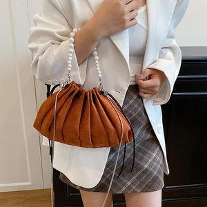 Brown suede pleated drawstring bucket bag with pearl handle worn by a model in casual suit
