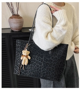 Detail of leopard print tote bag with plush bear charm worn by a model in a modern home