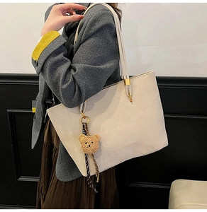 Grand sac cabas beige mat avec porte-clés ours, porté par un mannequin en blazer gris