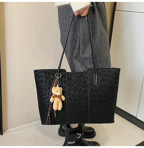 Detail of large leopard print tote bag with bear charm on a female model's shoulder