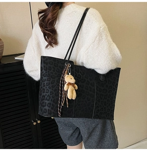 Detail of black leopard embossed tote bag with a cute brown plush bear charm