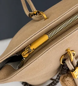 Vue macro d'une fermeture éclair dorée lisse sur un sac bandoulière en daim beige