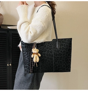 Detail of dark leopard print tote bag with plush bear charm worn on the shoulder