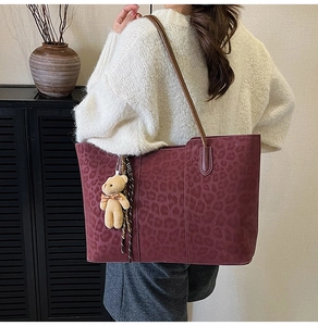 Detail of burgundy leopard print tote bag with brown plush bear charm and long shoulder strap