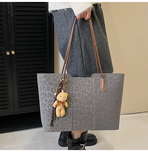 Detail of grey leopard print tote bag with brown leather straps and plush bear charm