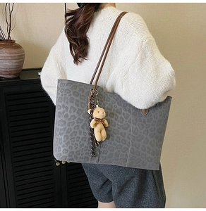 Detail view of large leopard print tote bag with plush bear charm and sleek brown shoulder strap