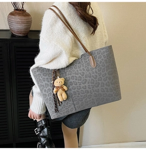 Detail of grey leopard print tote bag with brown straps and plush bear charm on model