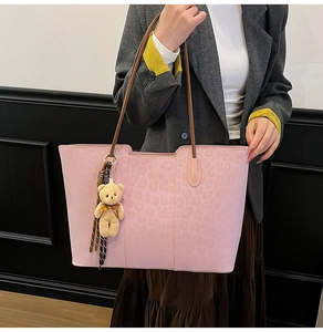 Detail of pink leopard embossed tote bag with brown handles and plush bear charm