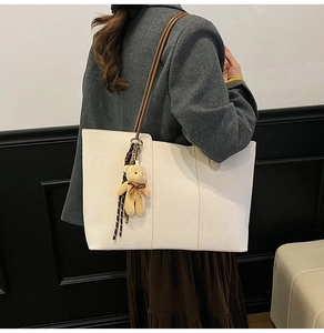Detail of cream tote bag with brown straps and plush bear pendant on model shoulder