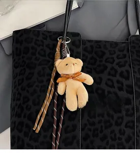 Close-up of fluffy bear bag charm with bow on leopard print tote bag accessory detail
