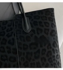 Detail of leopard print tote bag fabric with black textured leather handle reinforcement