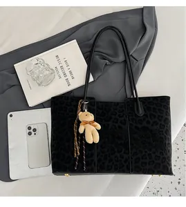 Large leopard print tote bag with plush bear charm showing capacity next to a tablet and book