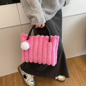 Pink plush tote bag with striped texture and black woven handles shown by a model