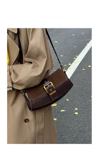 Detail of dark brown leather and suede baguette bag with a gold metal buckle on a shoulder strap