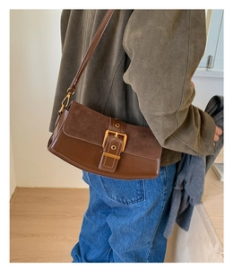 Detailed side view of brown crossbody baguette bag with gold buckle on a model