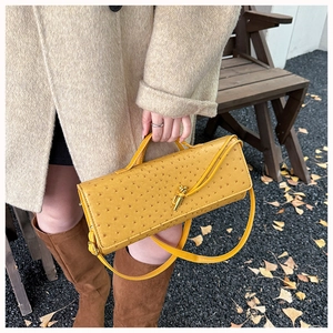 Detail of yellow ostrich texture handbag with golden latch lock in an autumn street setting
