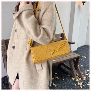 Detailed view of yellow ostrich texture shoulder bag with gold hardware worn on wool coat