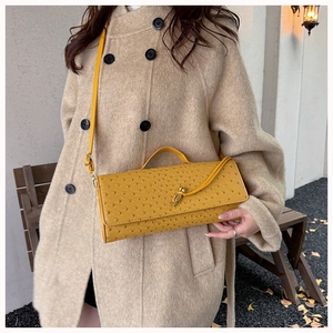 Detail of yellow ostrich texture handbag with gold metal clasp on a beige coat model