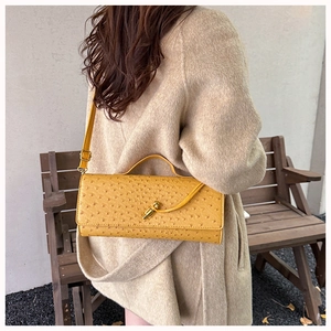 Detail of yellow ostrich pattern leather shoulder bag with gold metal clasp on a model