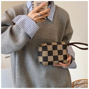 Detail van geruite clutch met bruine leren riem en gouden ritssluiting accenten