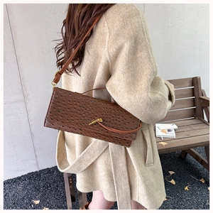 Detail of dark brown ostrich pattern shoulder bag with gold metal clasp on a beige coat