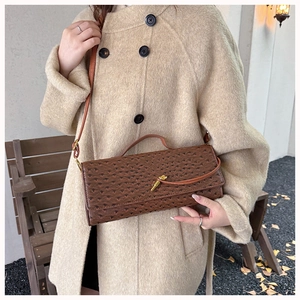 Brown ostrich-textured shoulder bag detail featuring a golden clasp and slim leather strap