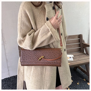 Close-up of deep brown ostrich-patterned leather baguette bag with a gold geometric lock
