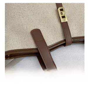 Close-up of contrast stitching and golden clasp on a beige canvas and brown leather tote