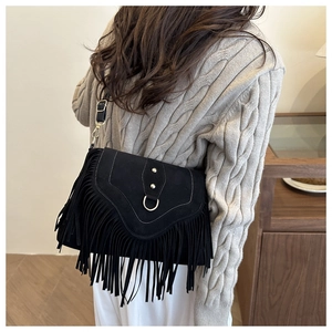Close-up of black fringe shoulder bag featuring matte suede texture and gold hardware