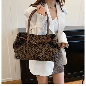 Detail of a large leopard print tote bag with brown leather straps and metal buckle accent