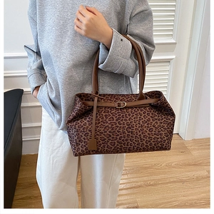 Detail of leopard print tote bag featuring brown leather straps and metal buckle decoration