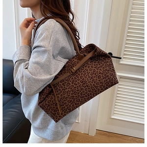 Detail of leopard print tote bag with brown leather handles worn by model in a room