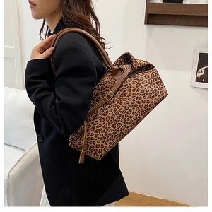 Detail of leopard print tote bag side with brown leather strap and metal buckle accent