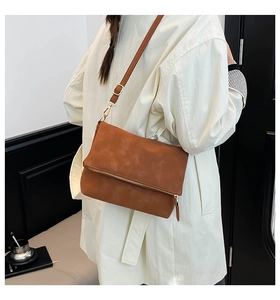 Detailed shot of brown faux suede envelope bag with gold hardware worn by model
