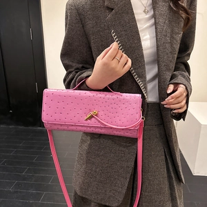 Pink ostrich pattern baguette shoulder bag with gold clasp shown on a tweed suit model