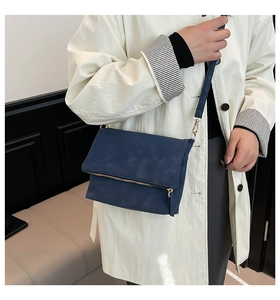 Detail of dark blue suede shoulder bag with gold hardware on a white coat model