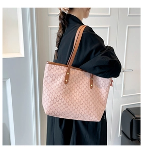 Detail of pink tote bag with M-pattern print and brown leather handles on shoulder